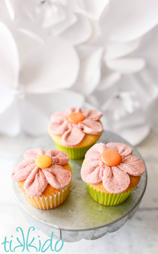 Vanilla cupcakes on a galvanized metal cake stand.  Cupcakes are frosted in all natural raspberry buttercream icing piped in the shape of a pink flower.