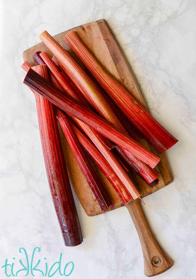 Stalks of red rhubarb on a wooden cutting board.
