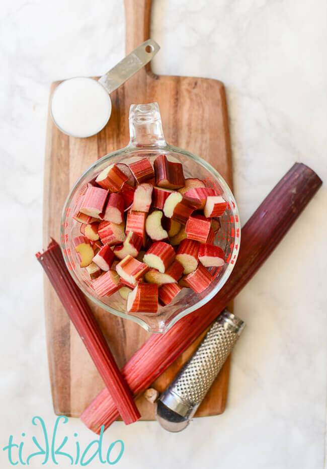 Rhubarb and sugar and a nutmeg grater on a cutting board, ingredients assembled to make rhubarb cobbler filling.