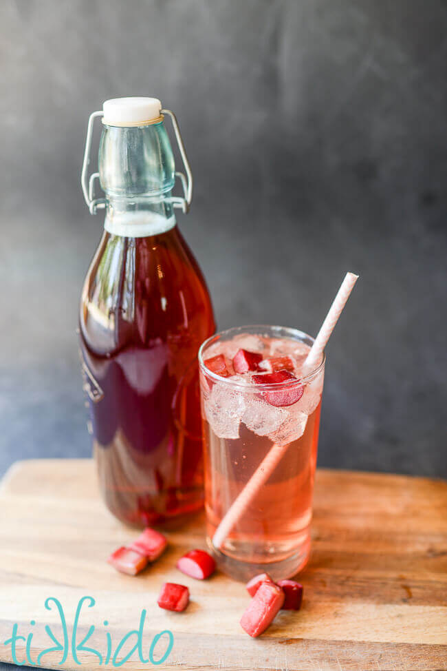 Rhubarb cocktail in a glass with a straw next to a glass bottle of Rhubarb Liqueur.