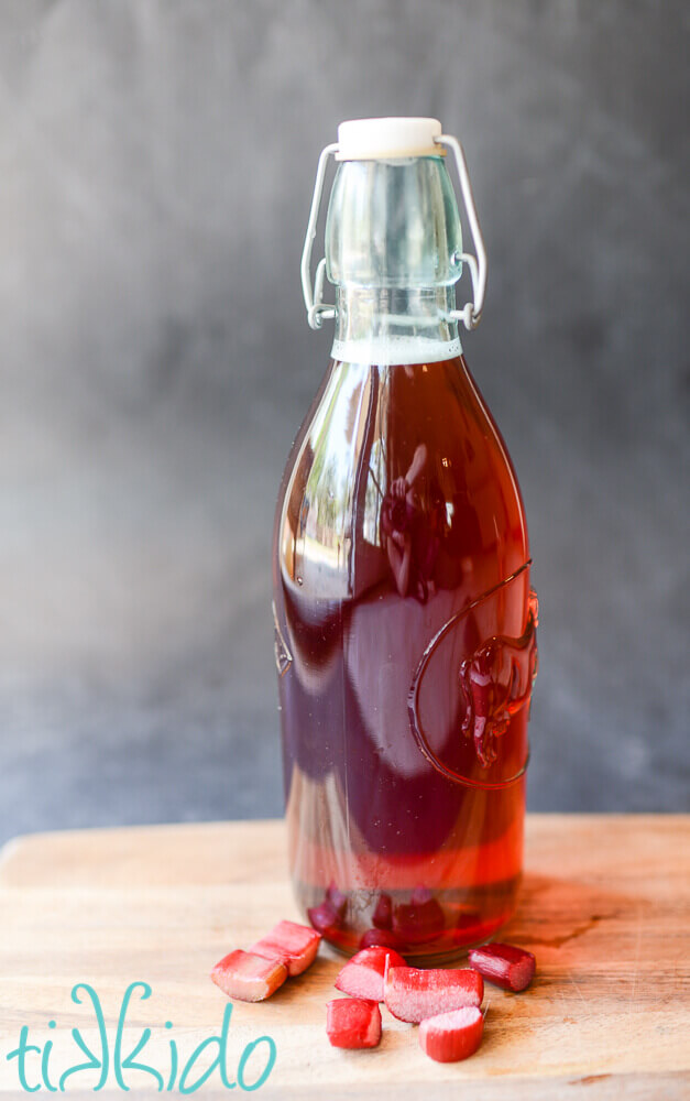 Homemade rhubarb liqueur in a glass bottle surrounded by pieces of fresh rhubarb.