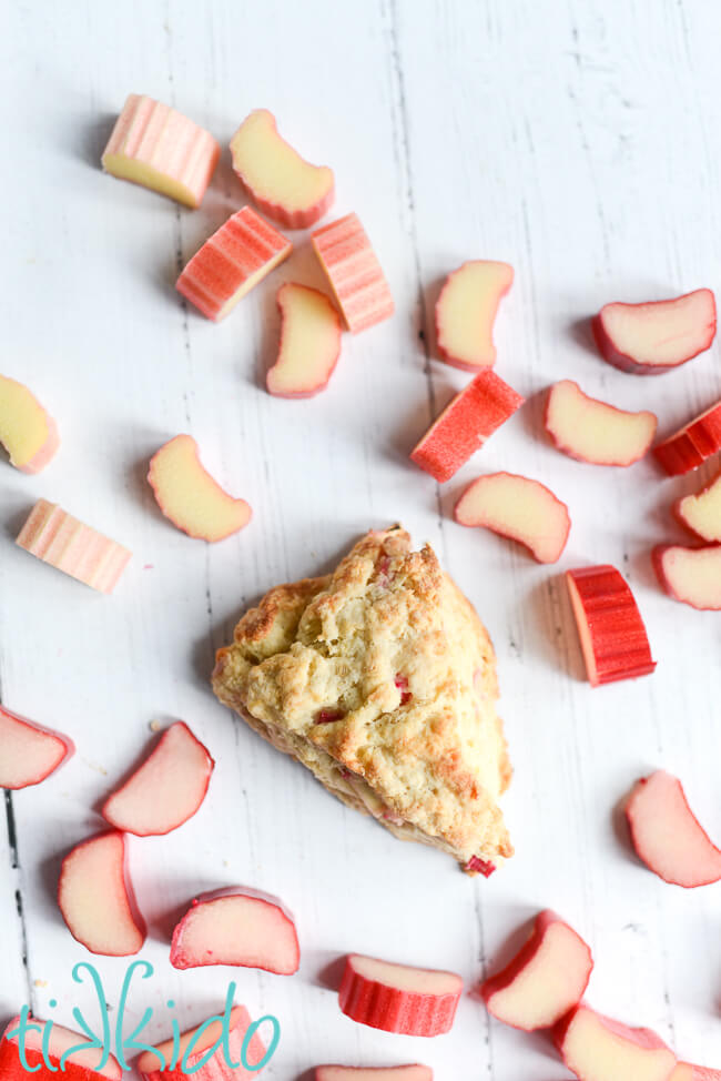 Rhubarb scone on a white wooden backdrop surrounded by slices of fresh rhubarb.