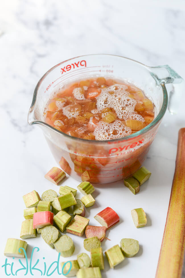 Rhubarb simple syrup before being strained, surrounded by fresh, chopped rhubarb.