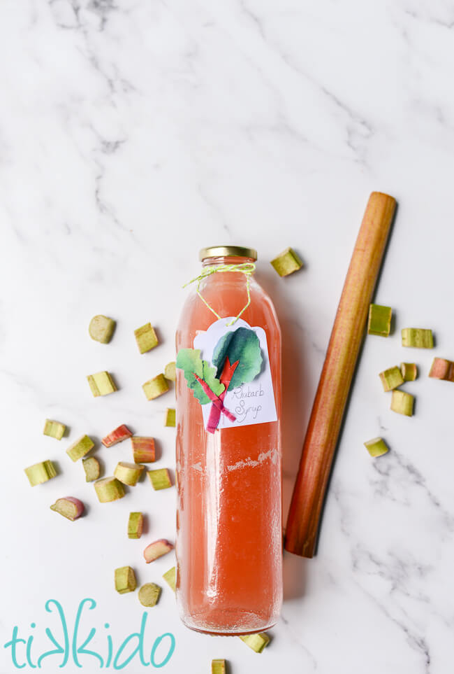 Rhubarb syrup in a glass bottle, surrounded by fresh rhubarb.