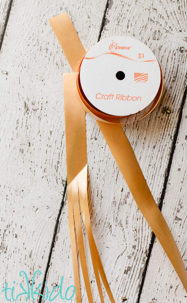 Golden craft ribbon spool and a piece of ribbon divided in four pieces on a white weathered wooden surface.