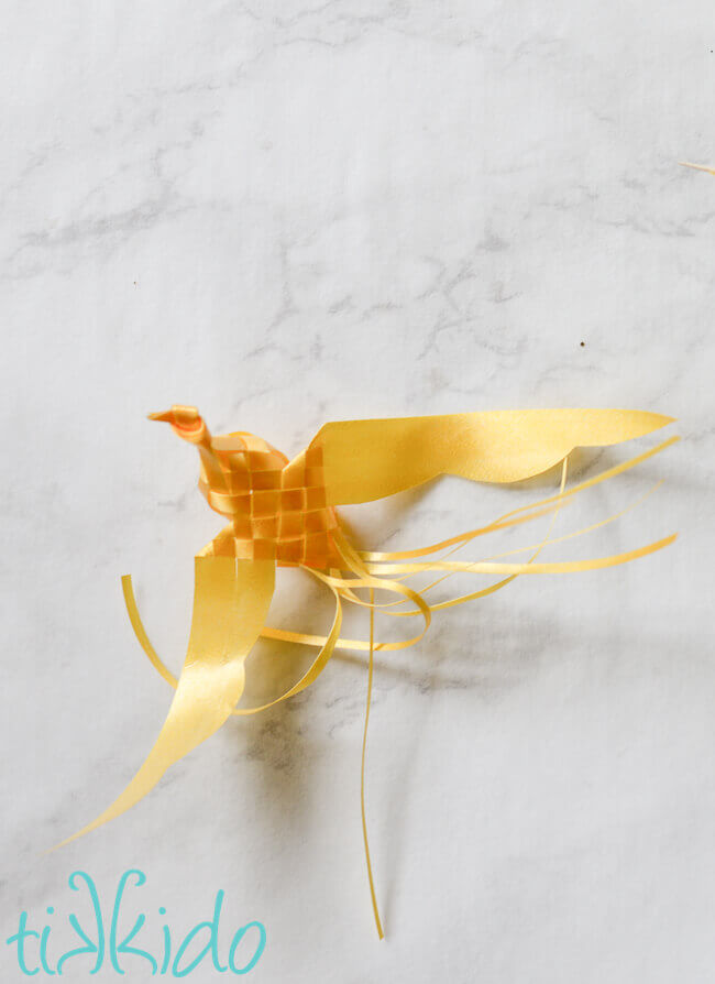  Yellow Woven Ribbon Bird on a white marble surface.