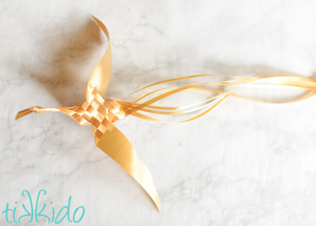  golden Woven Ribbon Bird on a white marble surface.