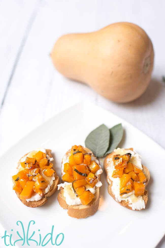 three slices of Butternut squash bruschetta with mascarpone, browned butter, and honey, on a white plate.