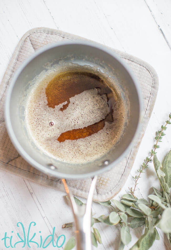 Small saucepan full of browned butter, on a white wooden surface surrounded by fresh sage and thyme.