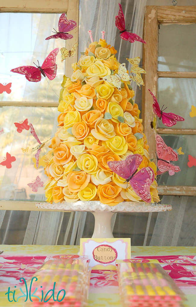 Fondant covered cake that looks like a tower of yellow roses,  surrounded by pink butterflies.
