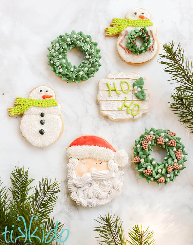 Santa, wreath, and snowman Christmas sugar cookies on a white marble surface.