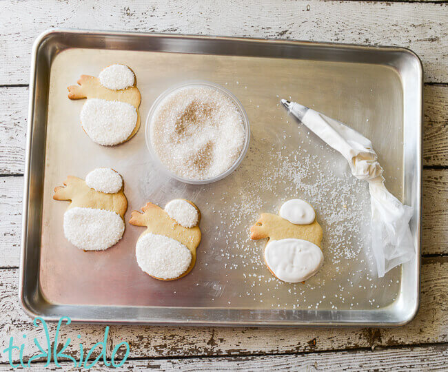 Snowman sugar cookies being decorated with white icing and coarse sugar.