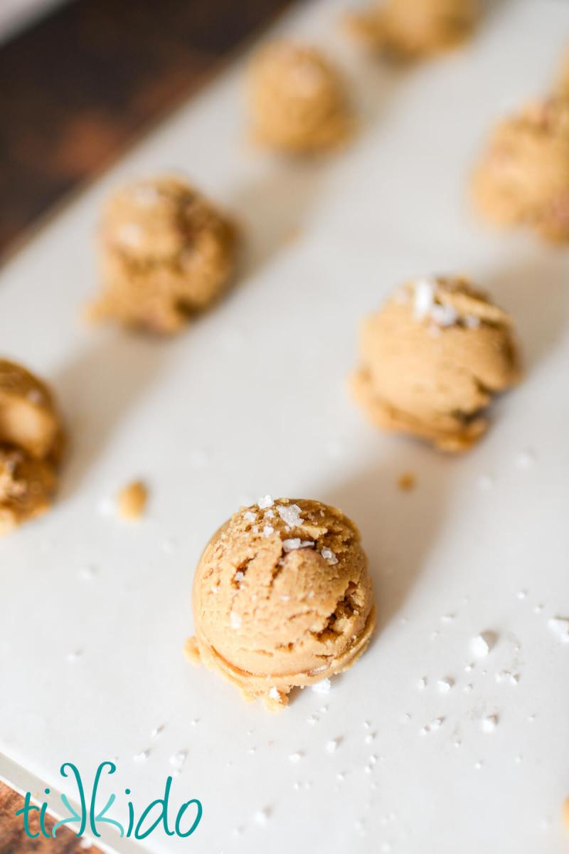 Unbaked salted caramel cookies sprinkled with sea salt flakes and ready to be put in the oven on a parchment lined cookie sheet.