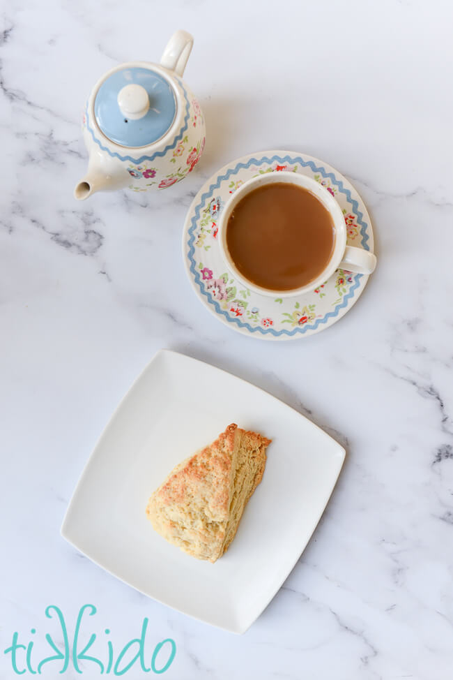 Scone made with an easy scones recipe on a white plate, next to a tea pot and cup of tea.