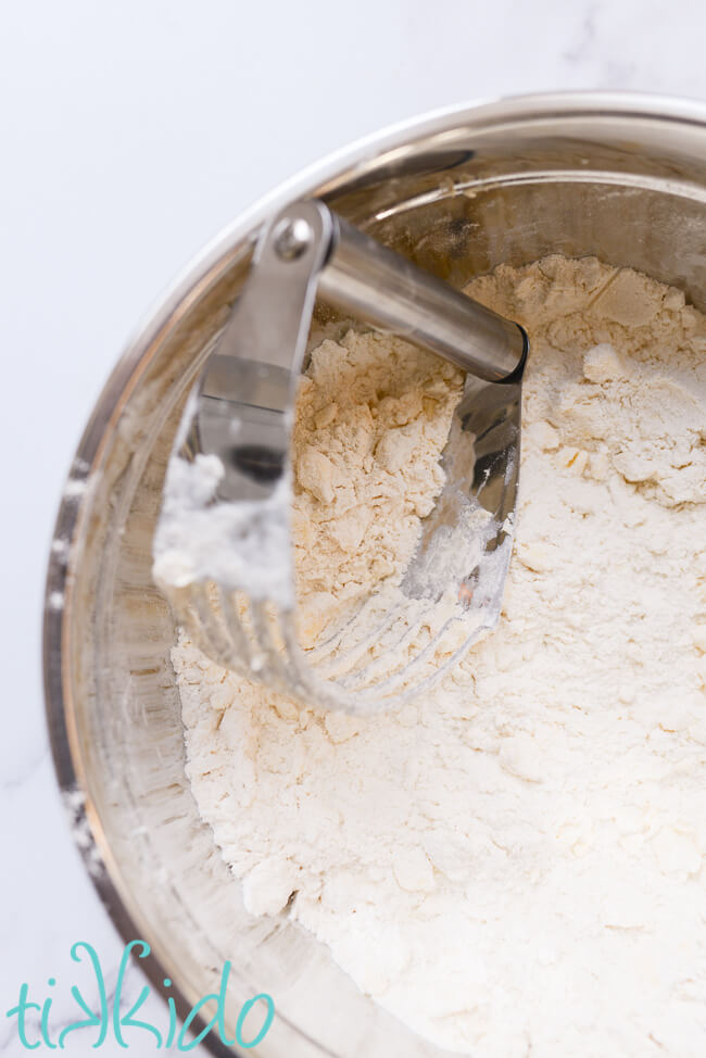 Silver bowl with flour mixture for making apple scones, with a pastry cutter that has been used to cut in the butter to the dry ingredients.