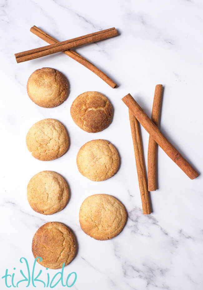 Snickerdoodle cookies next to cinnamon sticks on white marble.