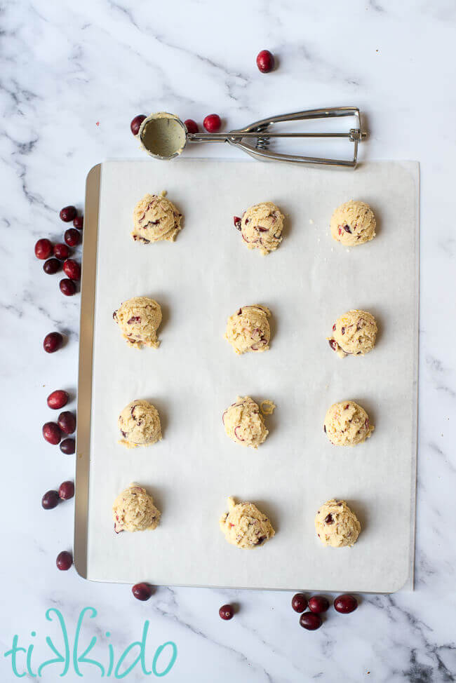 Cranberry cookie dough scooped out on a parchment lined baking sheet.