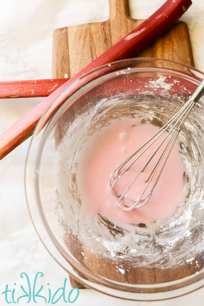 Rhubarb icing glaze mixed in a clear bowl with a whisk, for topping rhubarb cookies.