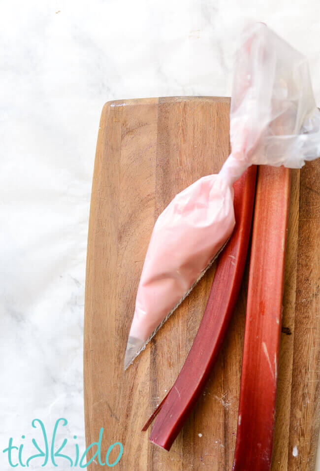 Rhubarb icing glaze in a piping bag next to fresh rhubarb stalks.