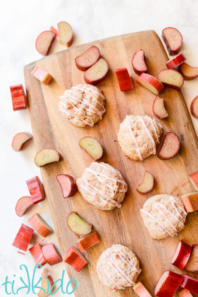 Soft rhubarb cookies on a wooden cutting board, surrounded by slices of fresh rhubarb.