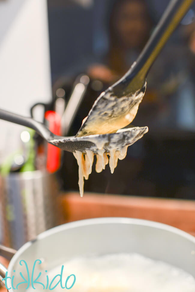 Homemade spaetzle being made by pushing spaetzle dough through a cooking spoon.