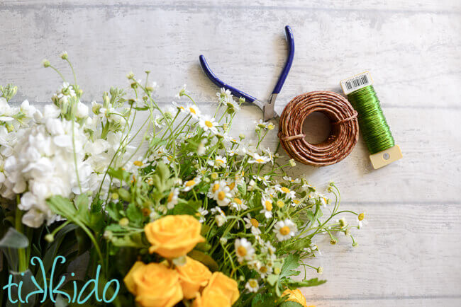 Fresh yellow and white flowers, wire cutters, and green and brown floral wire on a white background.