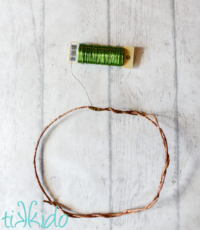 Brown floral wire twisted into a circle, green floral wire next to it on a white weathered wood table