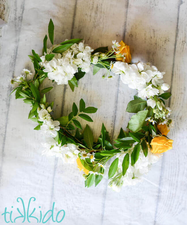 Overhead view of a real flower crown made from yellow and white flowers, sitting on a weathered white wood background.