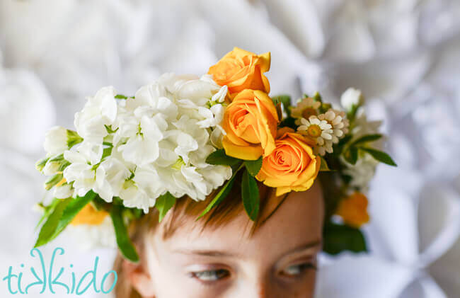 Little girl wearing a real flower crown made from yellow roses, chamomile flowers, and other white flowers.