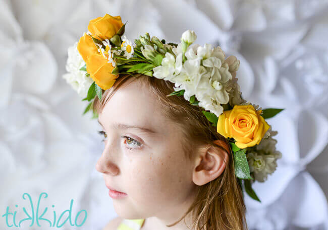 Little girl wearing a yellow and white real flower crown against a white background
