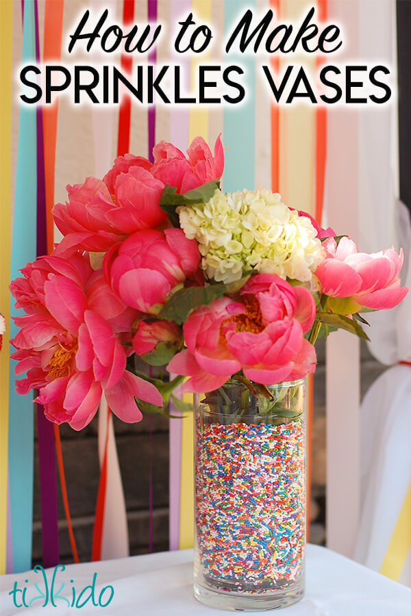 A vase filled with rainbow sprinkles and a pink and white flower arrangement, in front of a colorful ribbon backdrop, with text overlay reading "How to Make Sprinkles Vases."