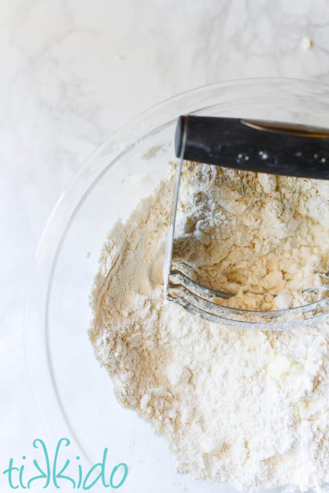 Butter being cut into dry ingredients for buttermilk biscuits in a clear pryex bowl.