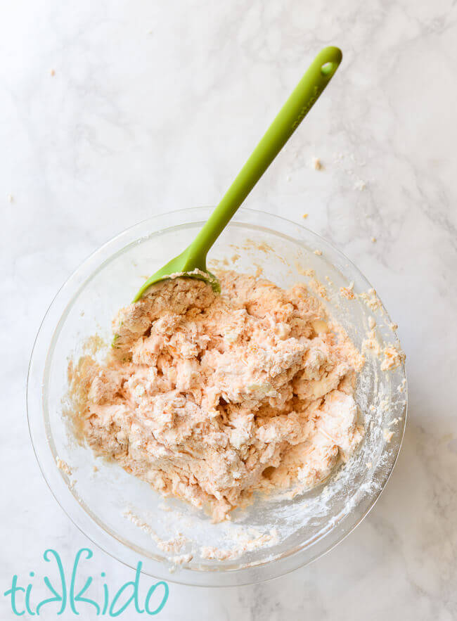 Sriracha Cheddar Biscuit dough in a clear bowl with a green spatula.