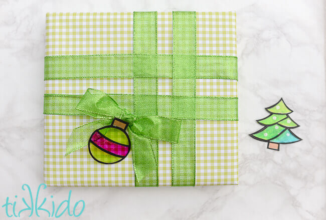 Ornament shaped green and pink faux stained glass gift tag on a present wrapped in green gingham and green ribbon.