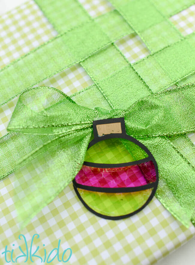 Ornament shaped green and pink faux stained glass gift tag on a present wrapped in green gingham and green ribbon.