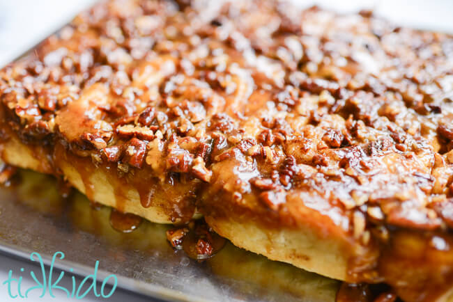 Tray of freshly baked sticky buns with warm caramel pecan sauce dripping down the side of the rolls.