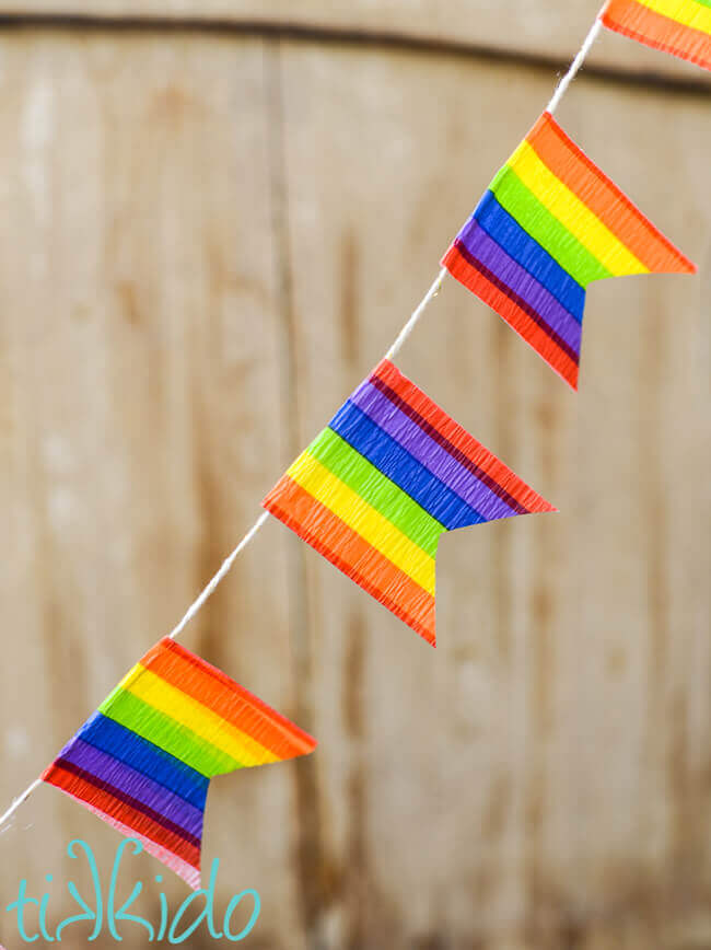Rainbow flag bunting made with rainbow crepe paper against a brown wooden backdrop