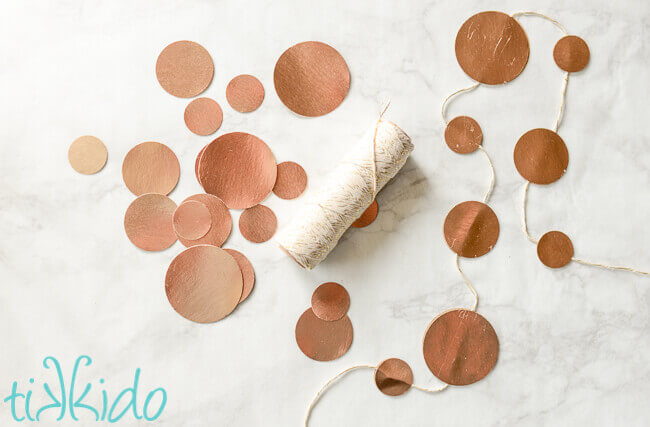 Gold circles of paper in various sizes, scattered on a white marble surface and glued to white and gold baker's twine.