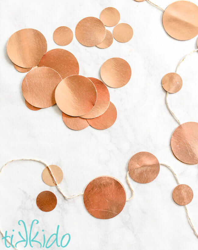 Gold circles of paper in various sizes, scattered on a white marble surface and glued to white and gold baker's twine.