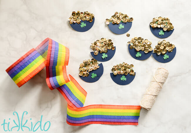 Pot of gold decorations, string, and rainbow crepe paper on white marble background