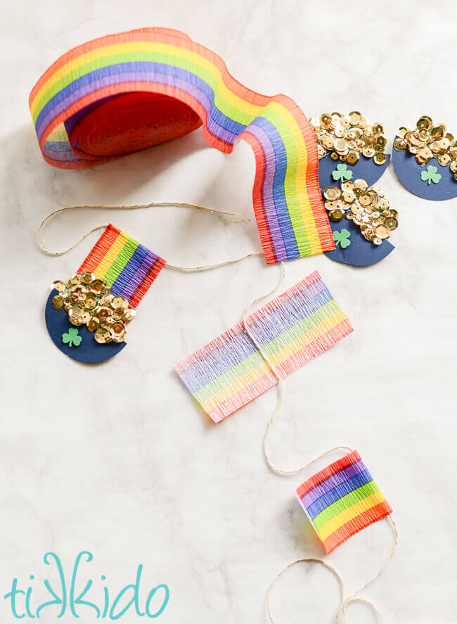 Progressive steps of assembling rainbow crepe paper and paper pots of gold on a St. Patrick's Day garland.