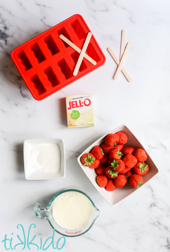 Ingredients for Strawberry Cheesecake Jello Pudding Pops Recipe on a white marble surface.