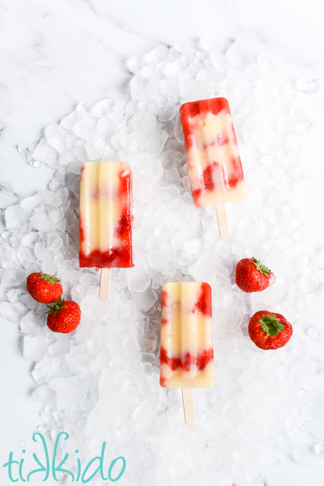 Three Strawberry Cheesecake Jello Pudding Pops on a bed of ice and fresh strawberries.