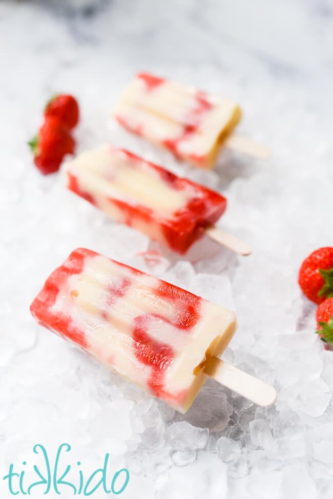 Three strawberry cheesecake jello pudding pops on a bed of ice and fresh strawberries.