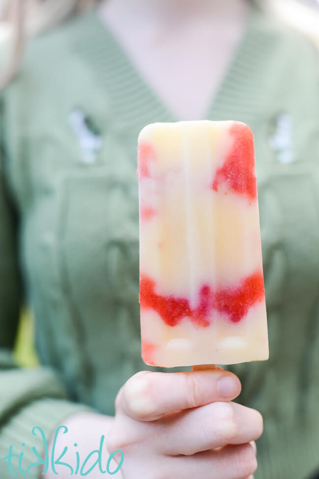 Woman wearing a green sweater holding a Strawberry Cheesecake Popsicle.