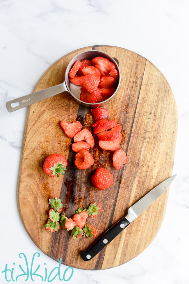 Strawberries being cut and hulled on a wooden cutting board.