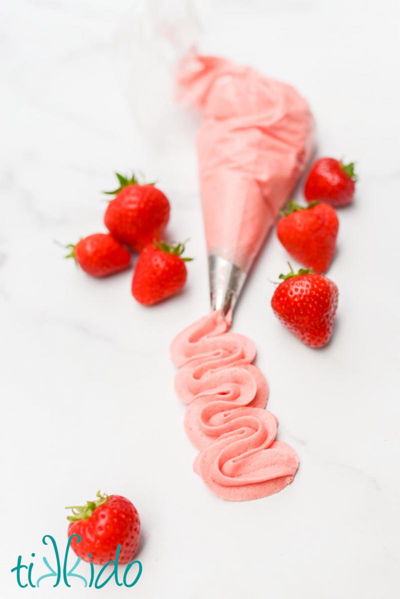 Strawberry Frosting piped out of a piping bag onto a marble surface, and surrounded by fresh strawberries.