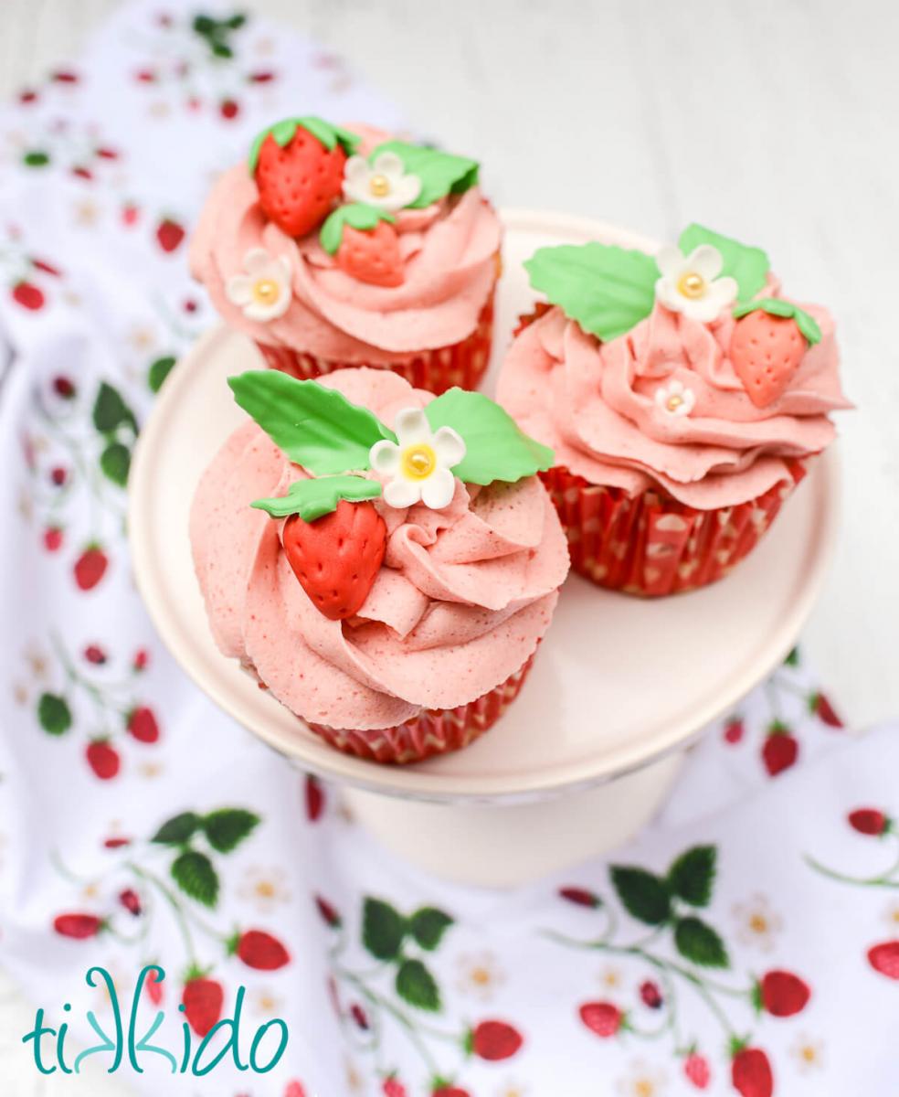 Three cupcakes topped with pink strawberry icing and gum paste strawberry decorations.