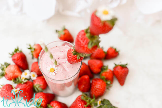 Strawberry milkshake surrounded by fresh strawberries on a white background.