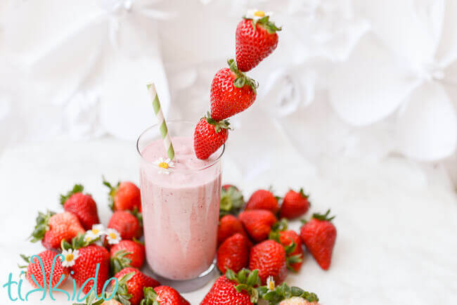 Strawberry milkshake surrounded by fresh strawberries on a white background.